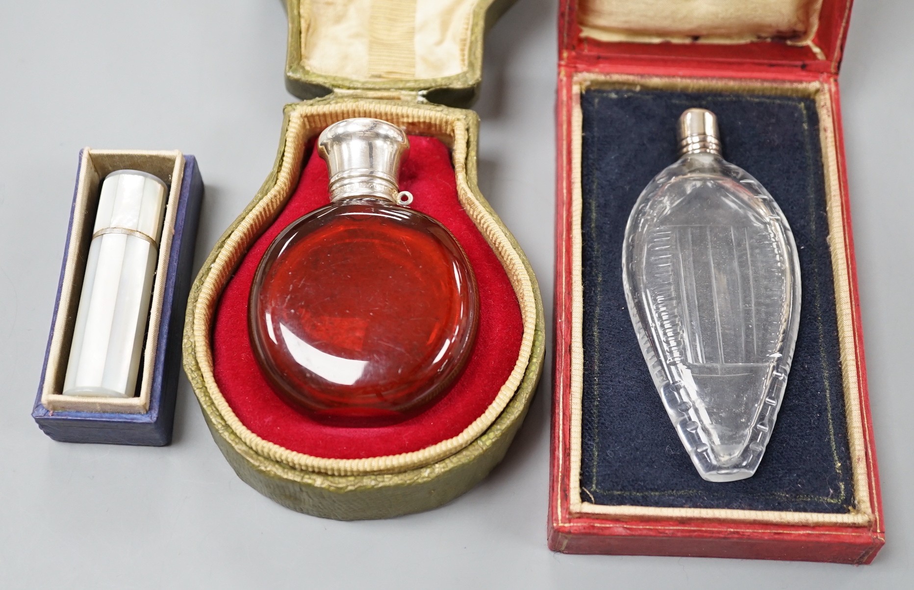 A cased Sampson Mordan white metal mounted ruby glass scent bottle, 7cm, one other mounted glass scent bottle and a mother of pearl mounted lipstick holder.